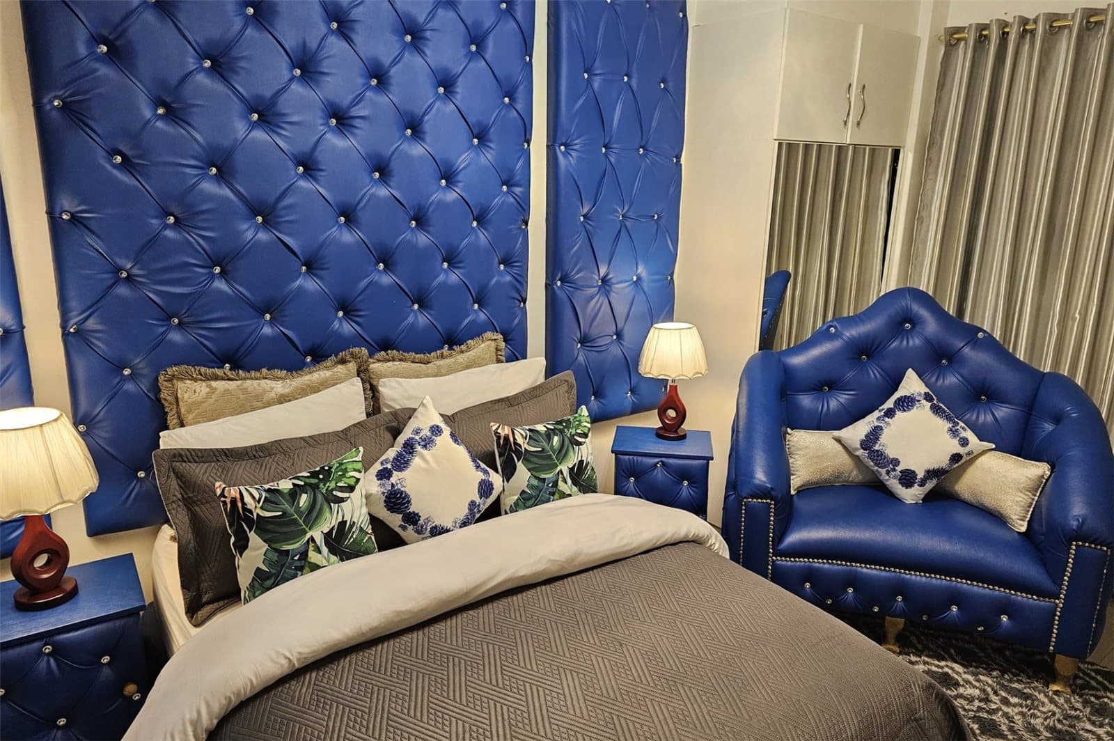 Studio suite with royal blue tufted headboard, armchair and warm bedside lamps