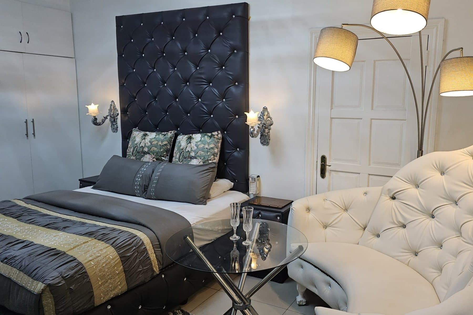 RJ's Guesthouse studio suite with black tufted headboard, warm lamps and lounge chair
